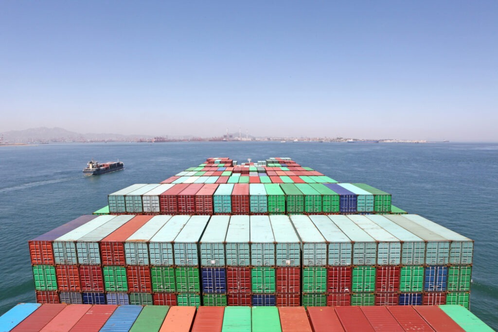 Colorful shipping containers stacked on a cargo ship, with a distant tanker navigating the blue waters under a clear sky, highlighting maritime trade.